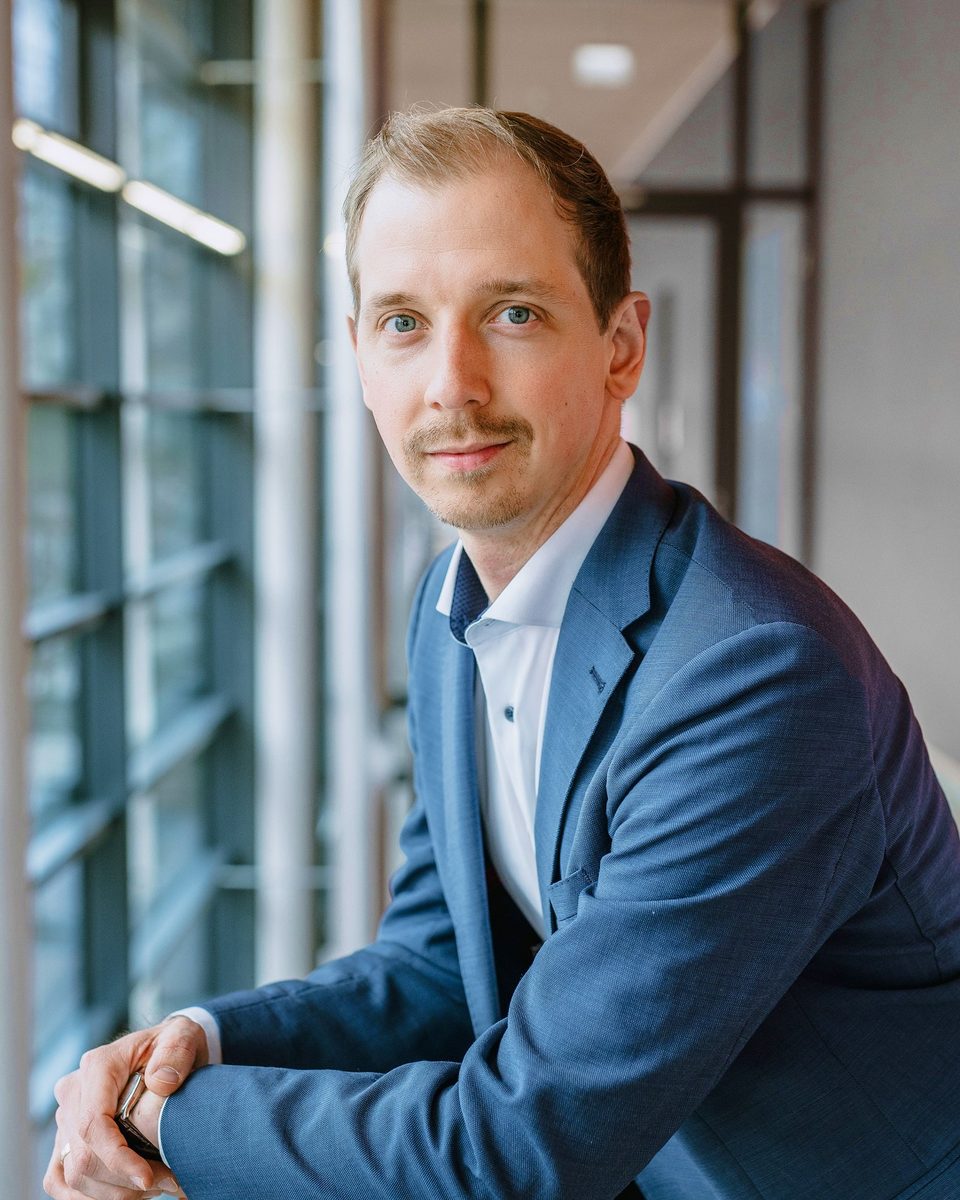 Portrait of Josua Decker in a blue jacket, leaning on a railing